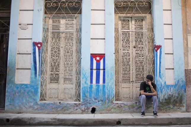 Un hombre sentado en una acera de La Habana, Cuba, con las banderas nacionales. 