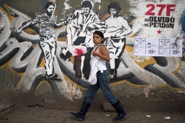A girl walks pass a wall painted with graffiti commemorating the social uprising