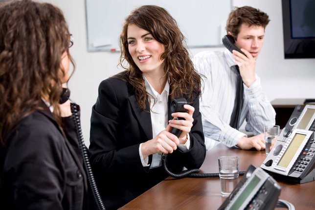 Call-Center. / Young happy customer service operators sitting in a row, holding 