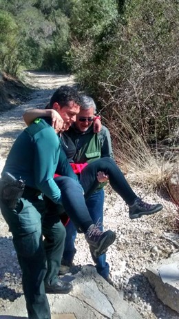 Un agente y un acompañante cargan con la mujer herida en el sendero.