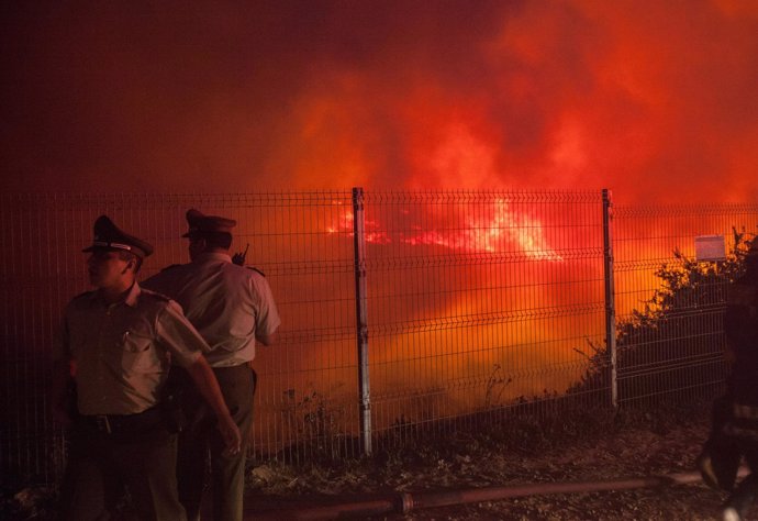 Police officers standby while a forest fire burns the hills of Valparaiso city