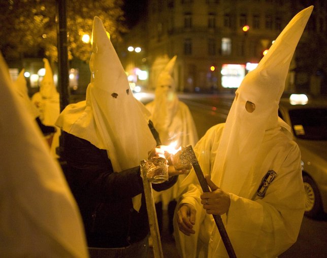 Supporters dressed as members of the Ku Klux Klan light flares as they express a