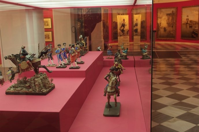 'Barros' Y Al Fondo Algunas De Las Pinturas Que Integran La Muestra De Unicaja.