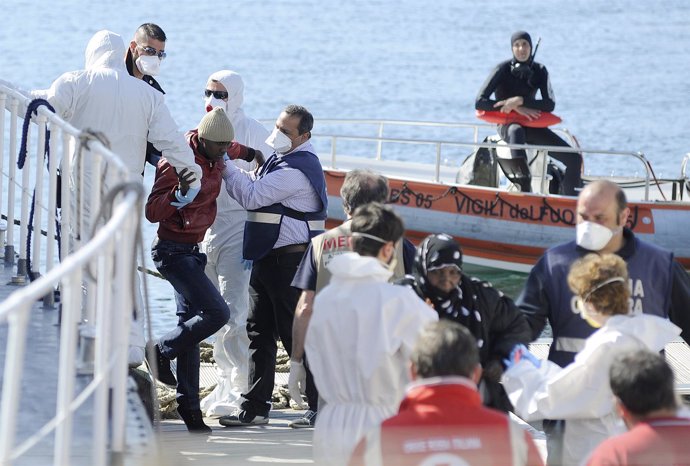 Migrants are helped as they disembark from a Coast Guard boat in the Sicilian ha