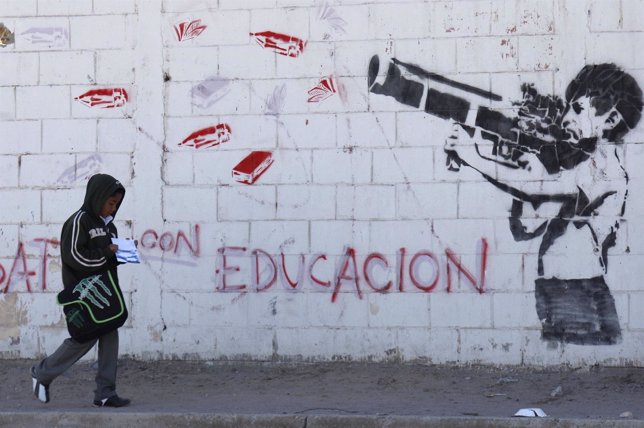 Un niño camina por Ciudad Juárez delante de mural con niño armado