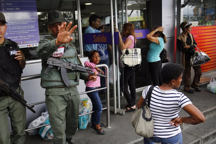 National guards stand a supermarket entrance as people line up outside in Caraca