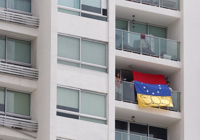 People hold a Venezuelan flag as a woman bangs a pot at the same time while Vene