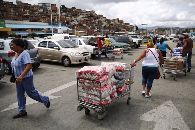 A woman pulls a cart with bags of rice outside Makro supermarket in Caracas