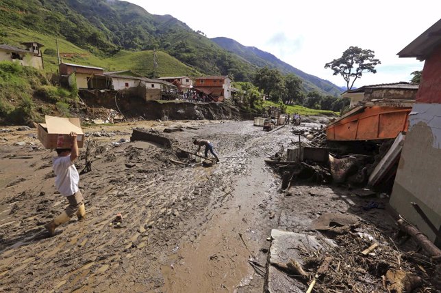 A resident carries supplies at the site where a landslide sent mud and water cra