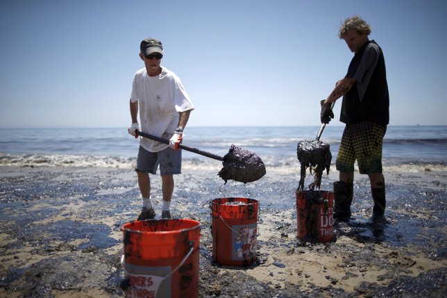 Volunteers carry buckets of oil from an oil slick along the coast of Refugio Sta