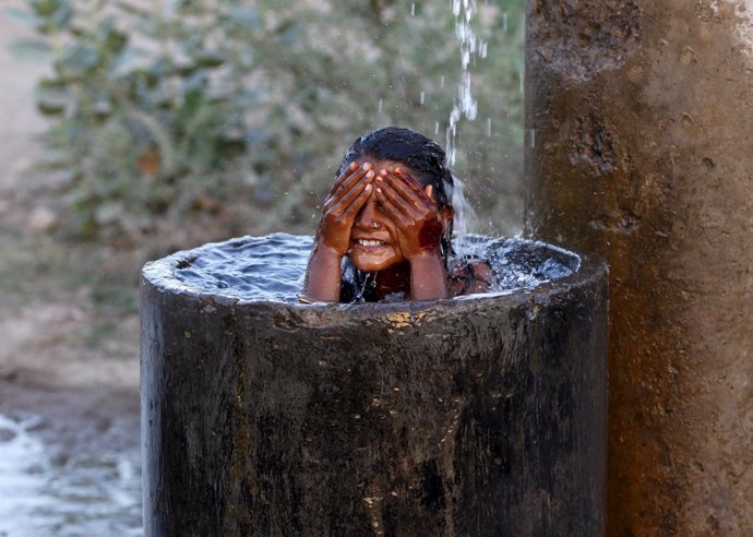 A girl bathes to cool off herself with water that is leaking from a broken pipe 