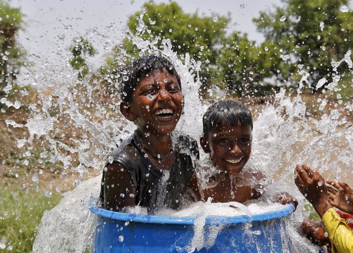 Dos niños alivian el calor en India bañándose en un contenedor