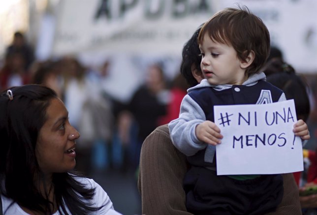 A woman looks at a boy that holds up a sign during a demonstration outside the C