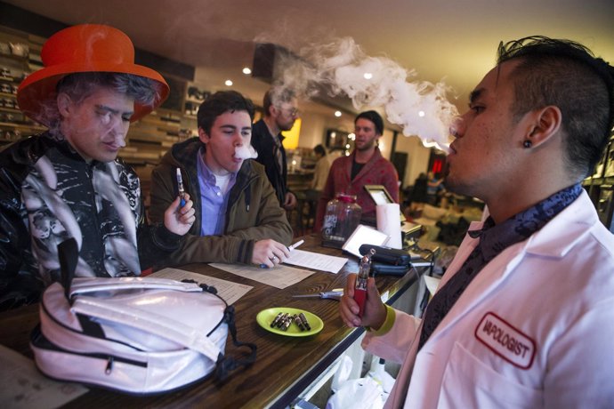 An employee "Vapologist" stands behind the bar as he puffs on an e-cigarette wit