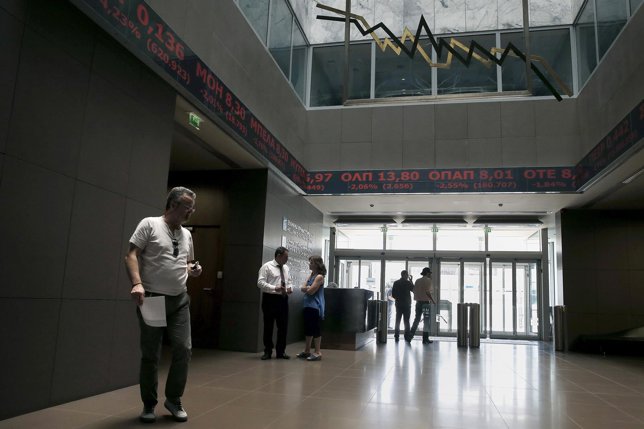 People walk inside the Athens stock exchange as a stock ticker shows stock optio
