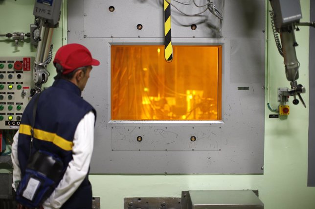 A worker looks through a thick glass window at part of the treatment of nuclear 