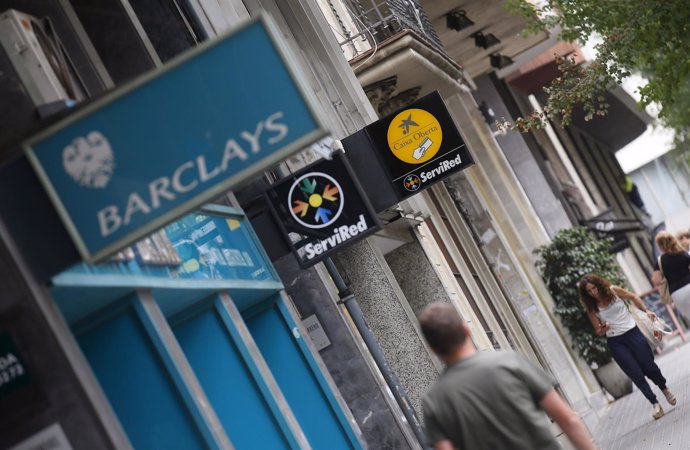 People walk past a LaCaixa and Barclays bank offices in Barcelona