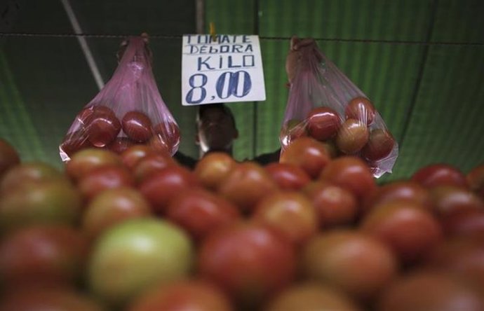 Un comerciante sostiene bolsas de tomate en su puesto del mercado de Sao Paulo. 