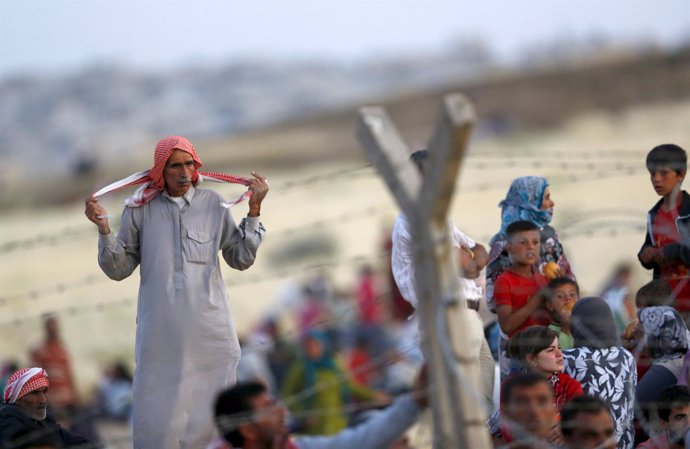 Syrian Kurds from Kobani wait behind the border fences to cross into Turkey as t