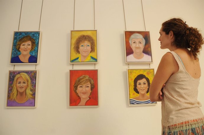 Un mujer observa varios cuadros de la muestra