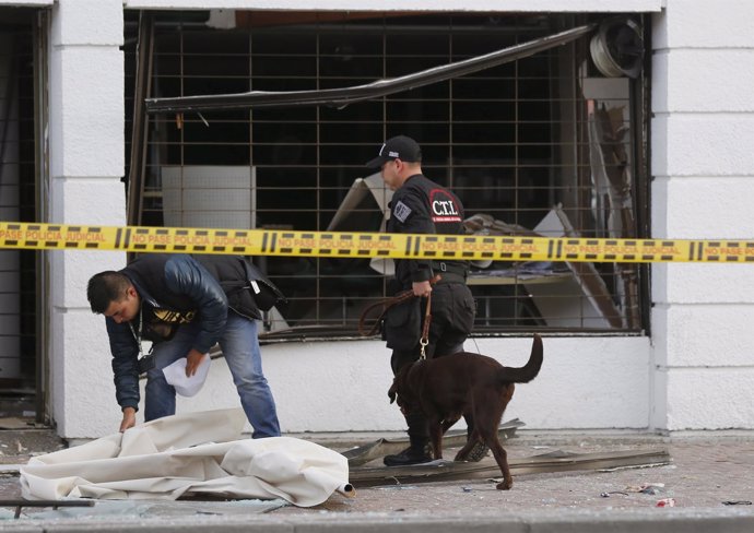 Policemen inspect the site of an explosion with a bomb sniffing dog, in front of