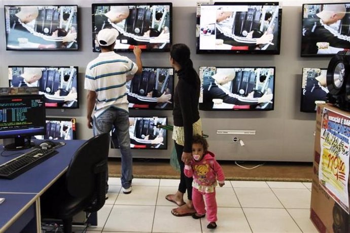 Una pareja junto a su hija miran televisores de pantalla planta en una tienda de