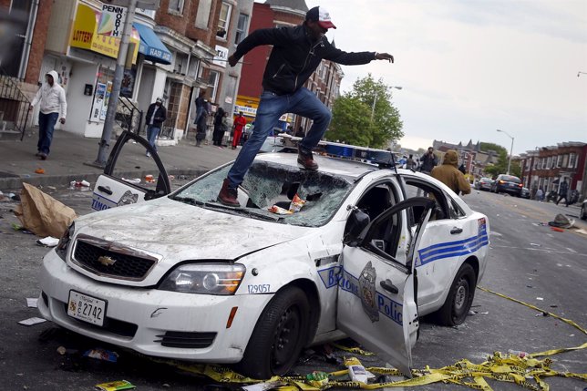 Demonstrators jump on a damaged Baltimore police department vehicle during clash