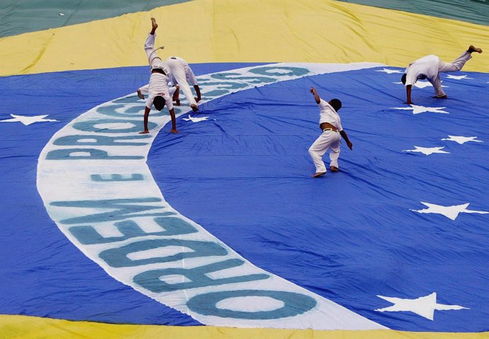 Niños haciendo Capoeira encima de una bandera gigante de Brasil.