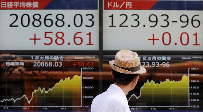 A man walks past in front of an electronic boards showing Japan's Nikkei average