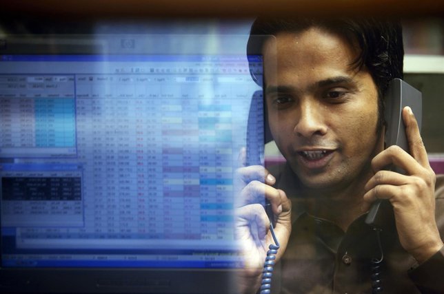 A computer screen displaying stocks is reflected in the window of a booth where 