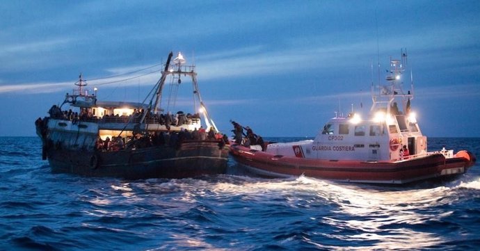 Patrullera de la Guardia Costera italiana junto a un barco con inmigrantes