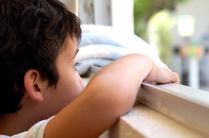 Autismo, niño mirando por la ventana.