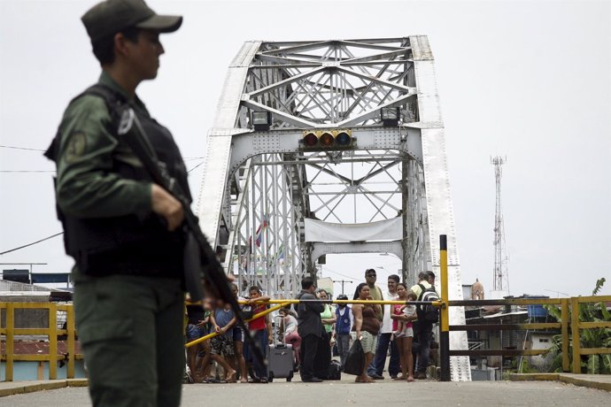 People stand next to a closed gate while a Venezuelan soldier stands guard at La