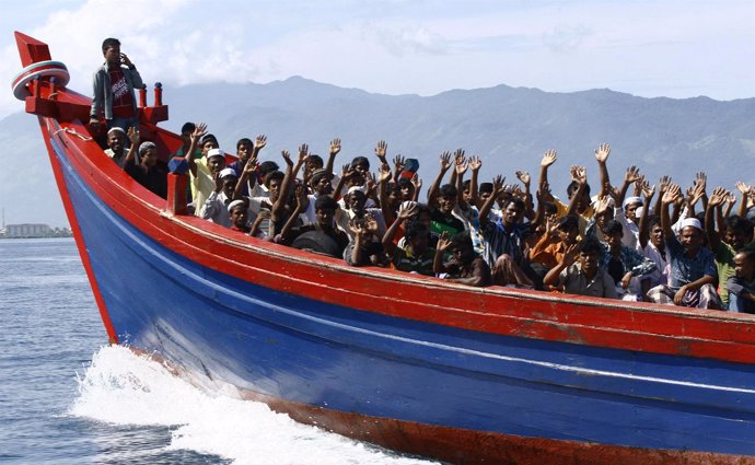 Ethnic Rohingya refugees from Myanmar wave as they are transported by a wooden b