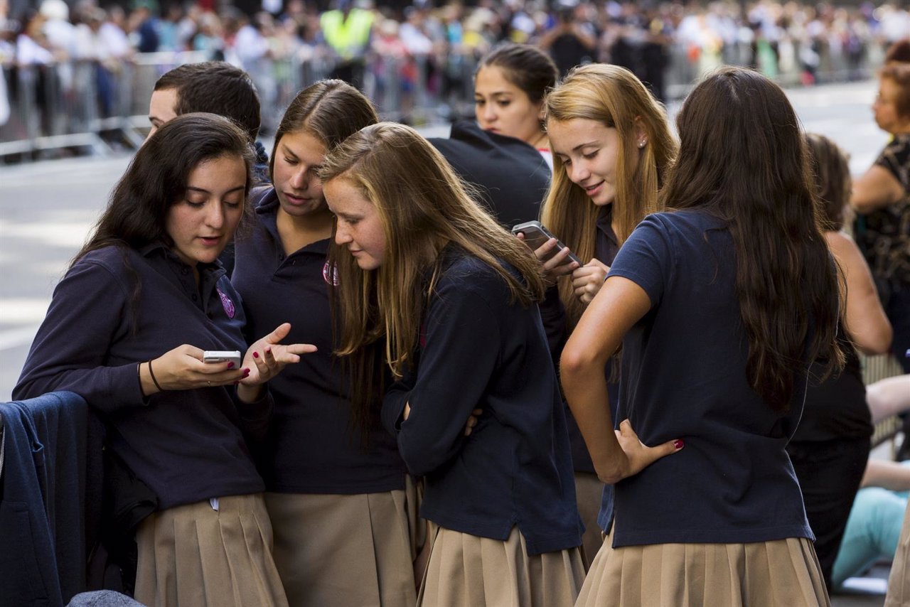 A group of Catholic school girls look at their phones as they wait on the route 