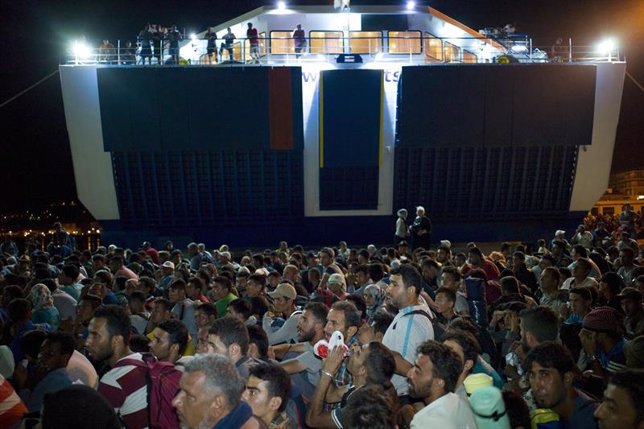 Refugees and migrants wait to board the passenger 