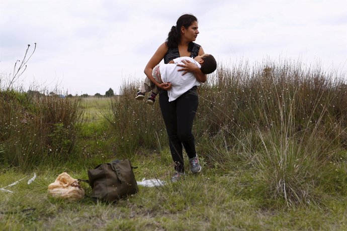 A Salvadoran immigrant carries her son while standing in vegetation to hide from
