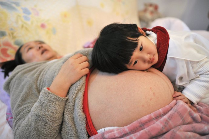 Niña china apoyada en la barriga de su madre.