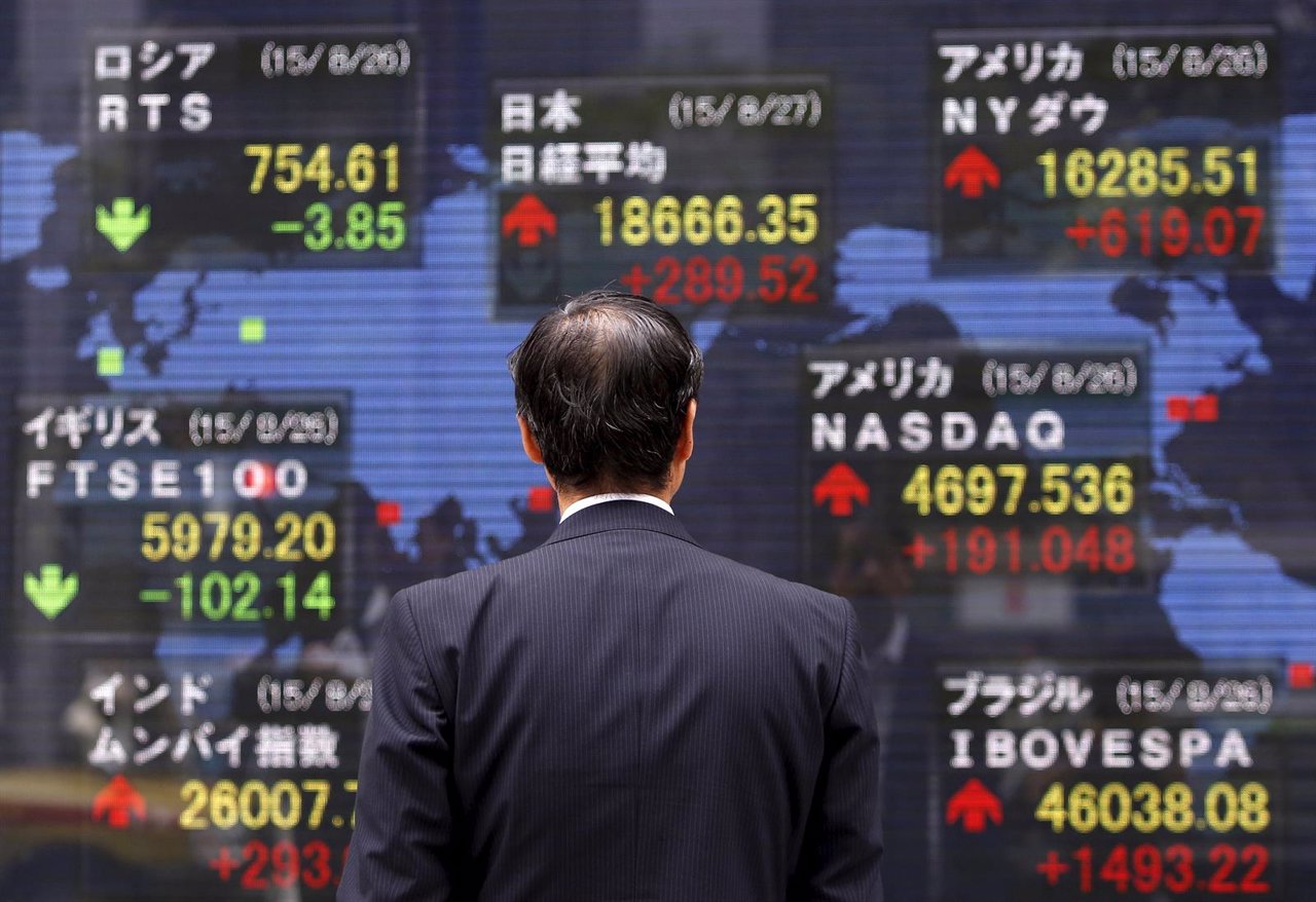 A pedestrian looks at an electronic board showing the stock market indices of va