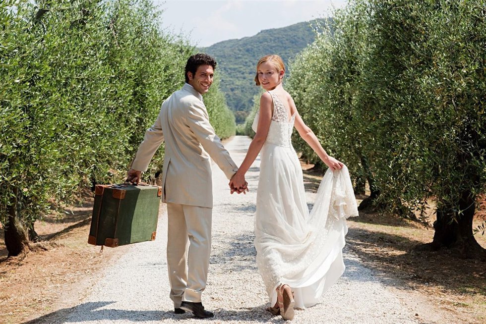 Newlyweds walking on country road with suitcase
