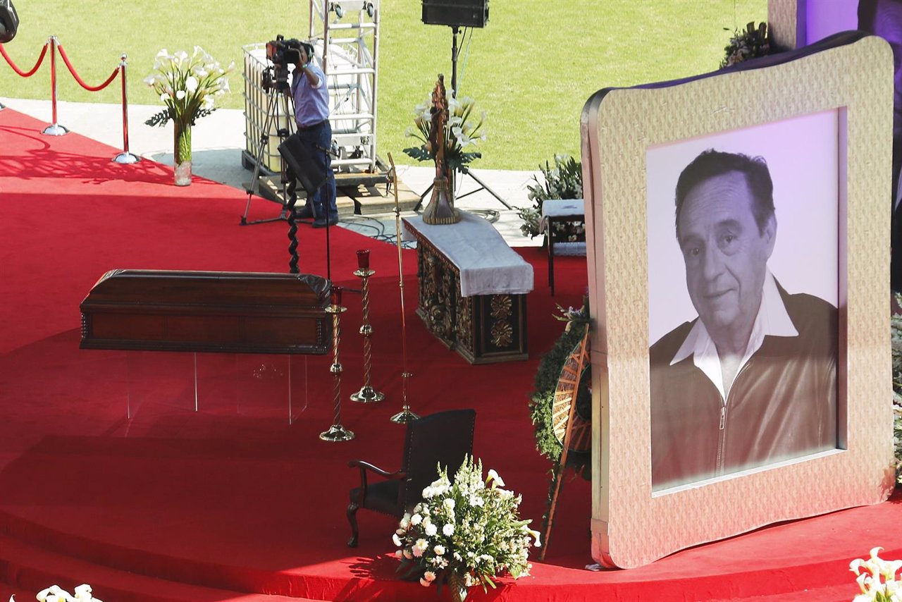 The coffin of the late screenwriter Chespirito is seen next to a giant picture o