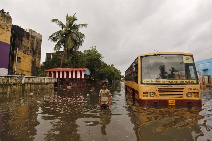 A boy wades next to a partially submerged bus in a flooded locality in Chennai