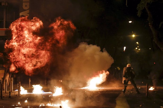 A petrol bomb explodes next to a riot police officer during clashes with hooded 