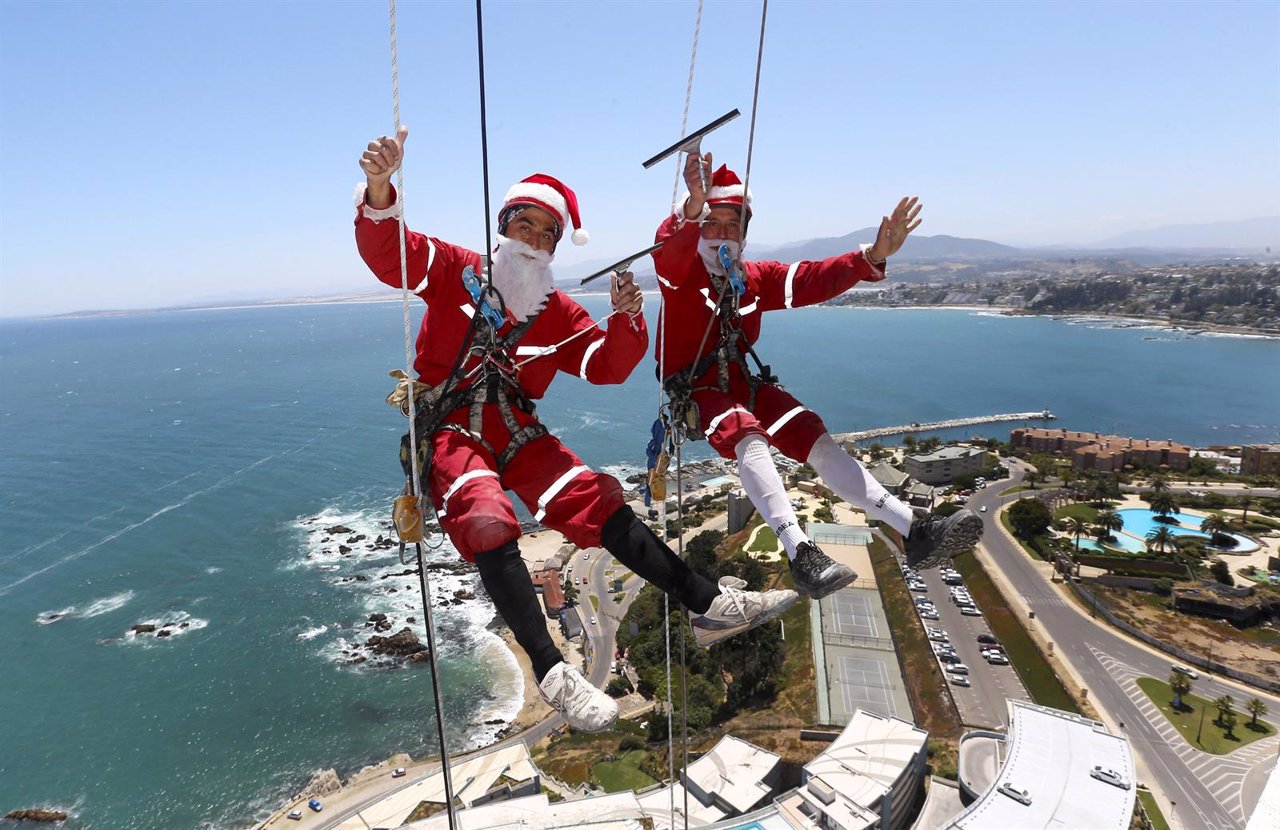 Workers wave as they clean the windows of a building, dressed as Santa Claus, in