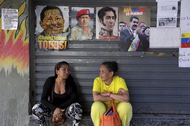 Women talk while seated under images of Venezuela's late President Chavez, natio