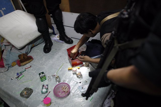 Thai policemen search the home of a suspected drug dealer during a pre-dawn raid