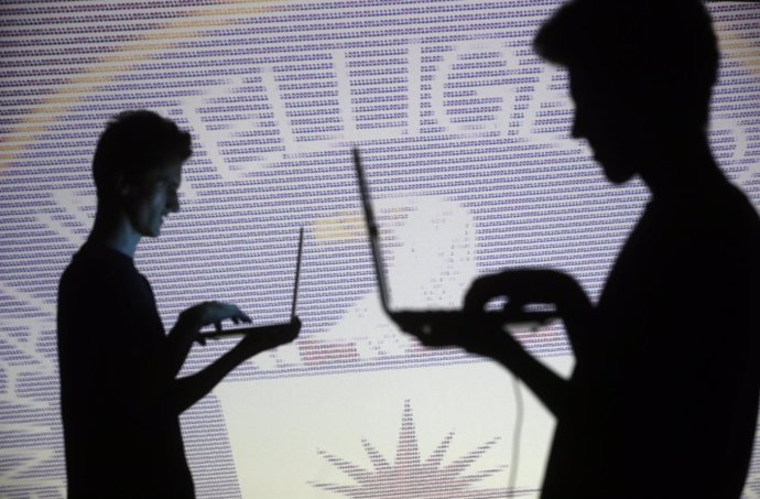 People pose with laptops in front of projection of  binary code and CIA emblem i