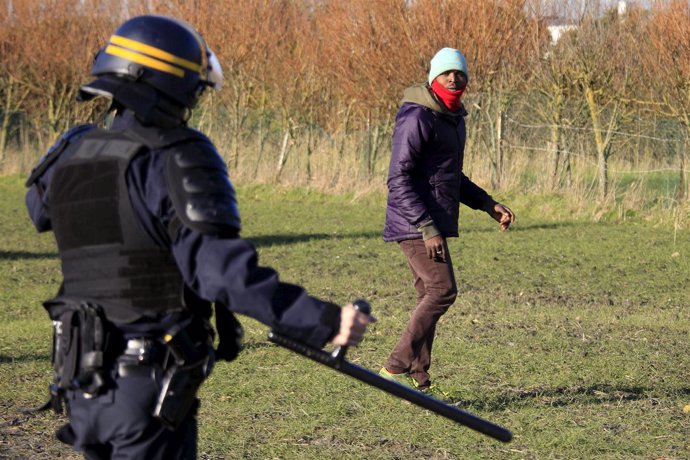 Policía con una porra frente a un inmigrante en Calais
