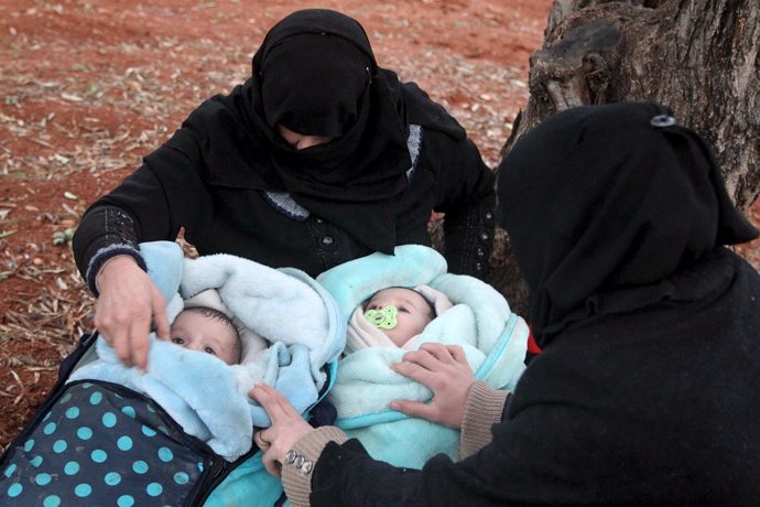 Dos mujeres esperan con sus bebés a cruzar desde Siria a Turquía