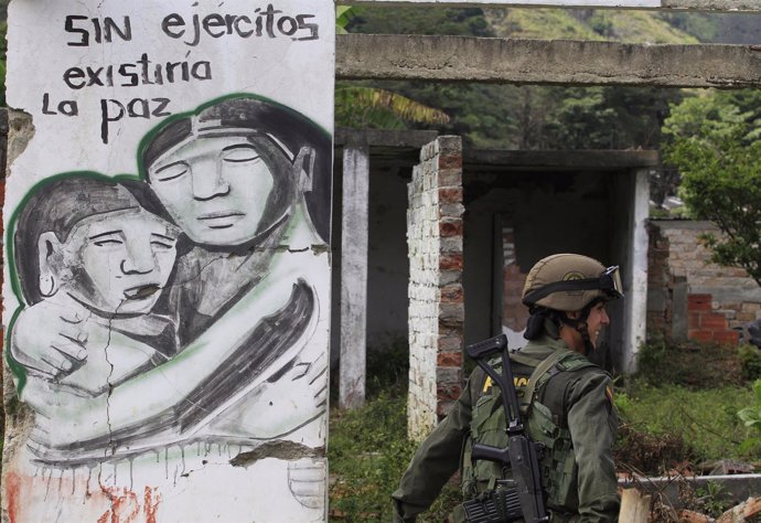 A Colombian police officer walks by a mural that reads "peace will exist without